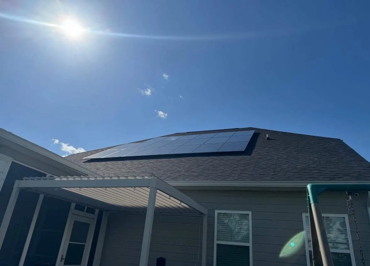 Solar panels on an asphalt-shingle roof under a clear blue sky