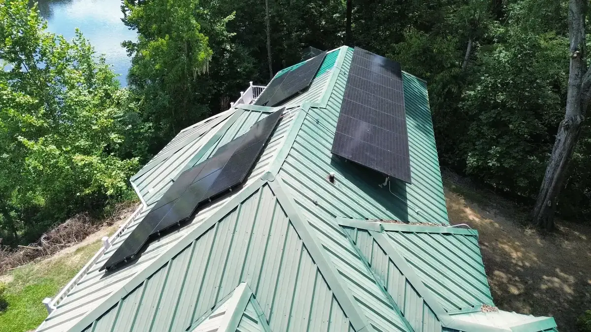 Aerial view of solar panels on a green standing-seam metal roof by a lake