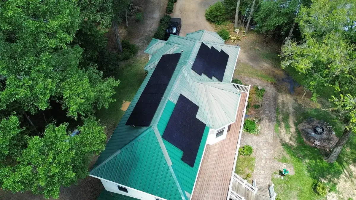 Top-down aerial view of solar panels across a green metal roof in the woods