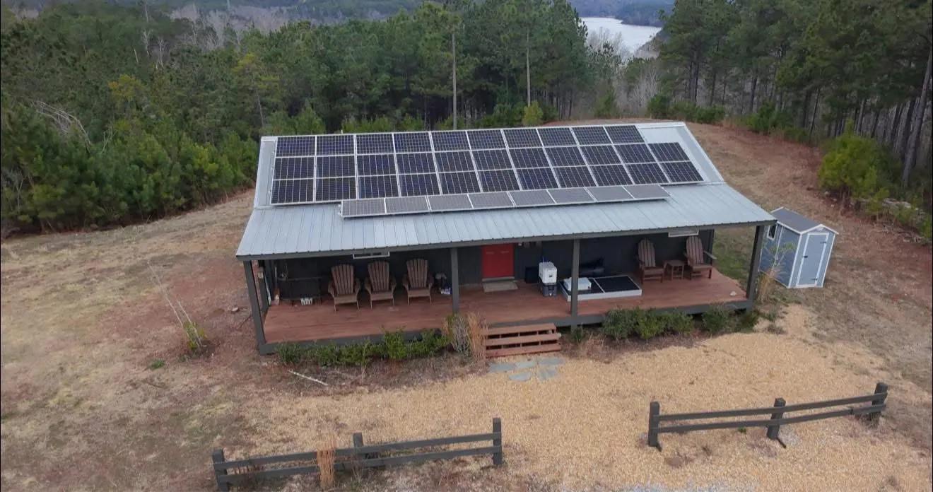 Off-grid cabin with a full roof solar array and a lake view behind it